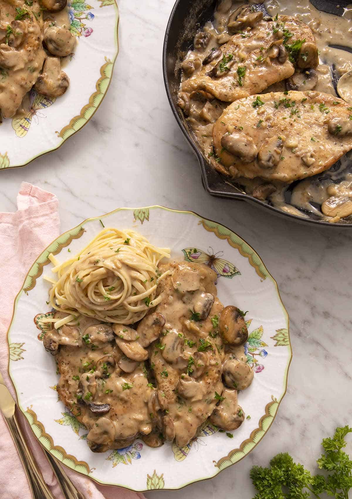 Two plates of chicken marsala on a marble counter.