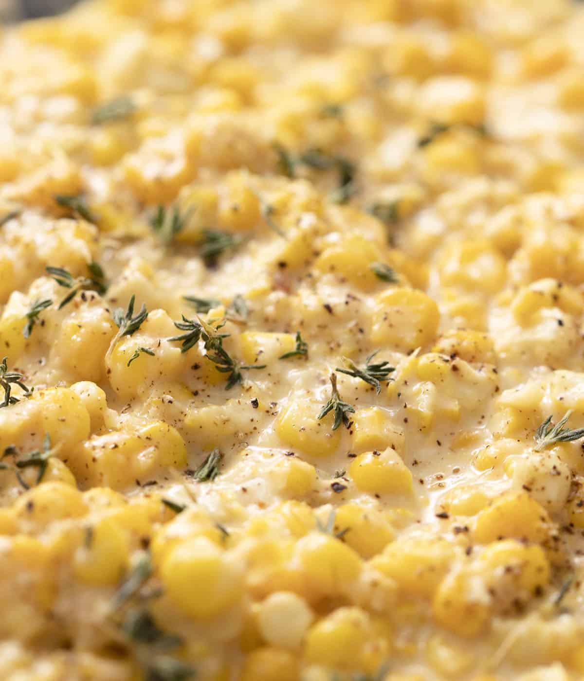 A cloeup photo of creamed corn flecked with thyme and black pepper.