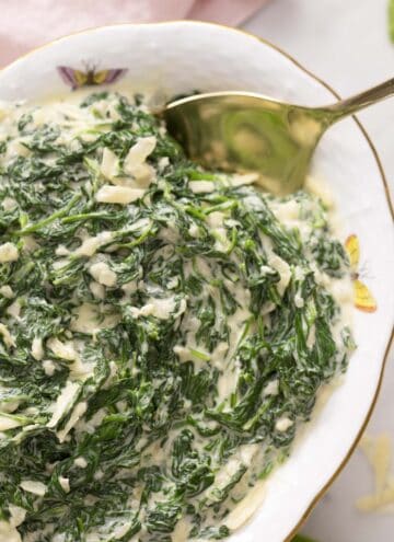 An oval porcelain bowl filled with creamed spinach.