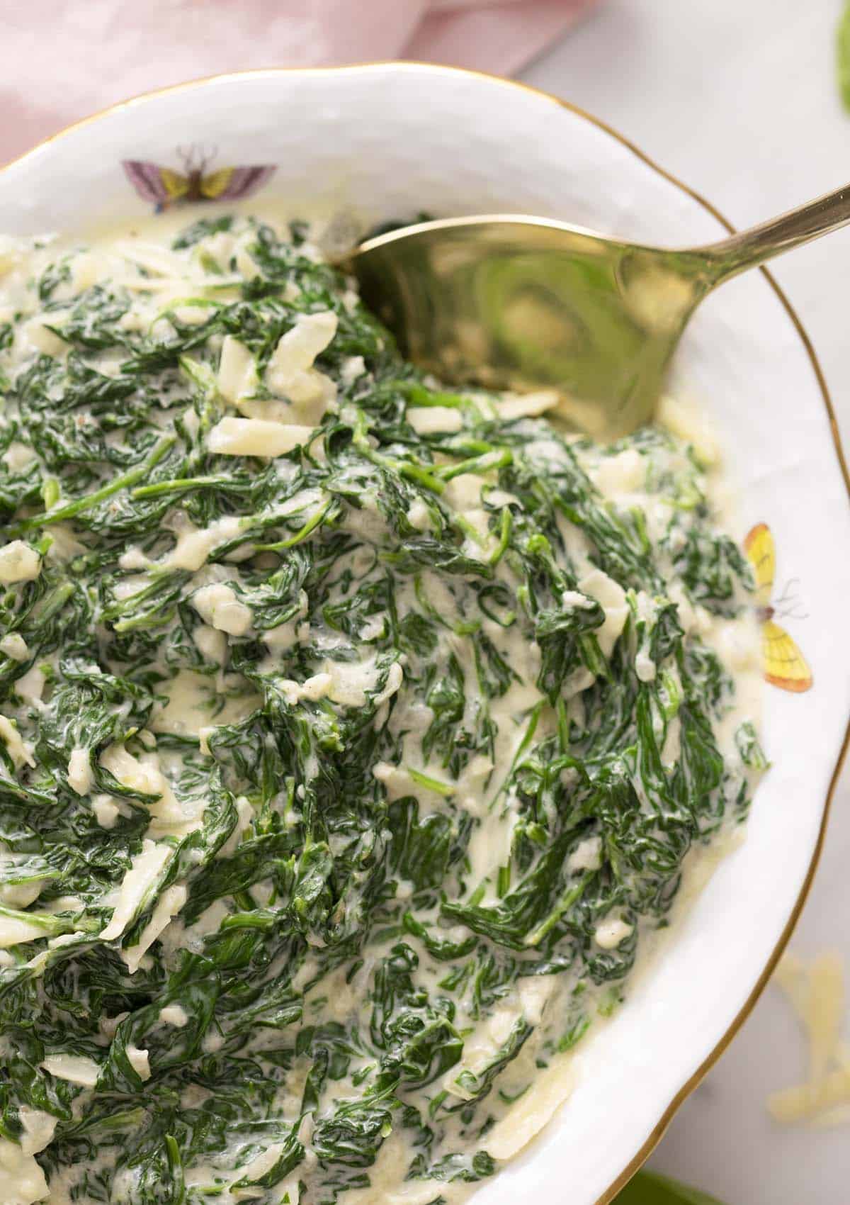 An oval porcelain bowl filled with creamed spinach.