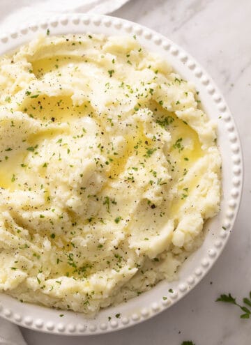 Mashed potatoes with parsley, black pepper, and melted butter in a white serving dish.