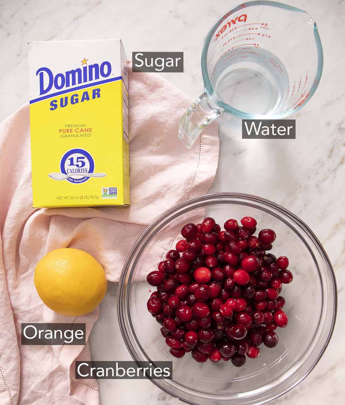 Ingredients to make cranberry sauce on a marble counter.