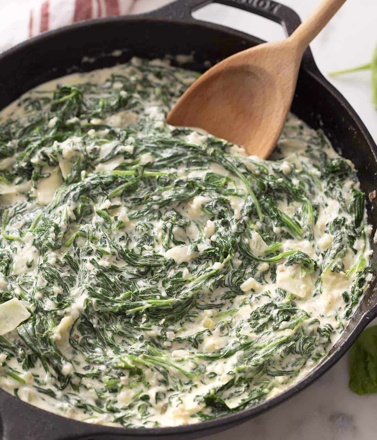 A wooden spoon in a skillet of homemade creamed spinach.