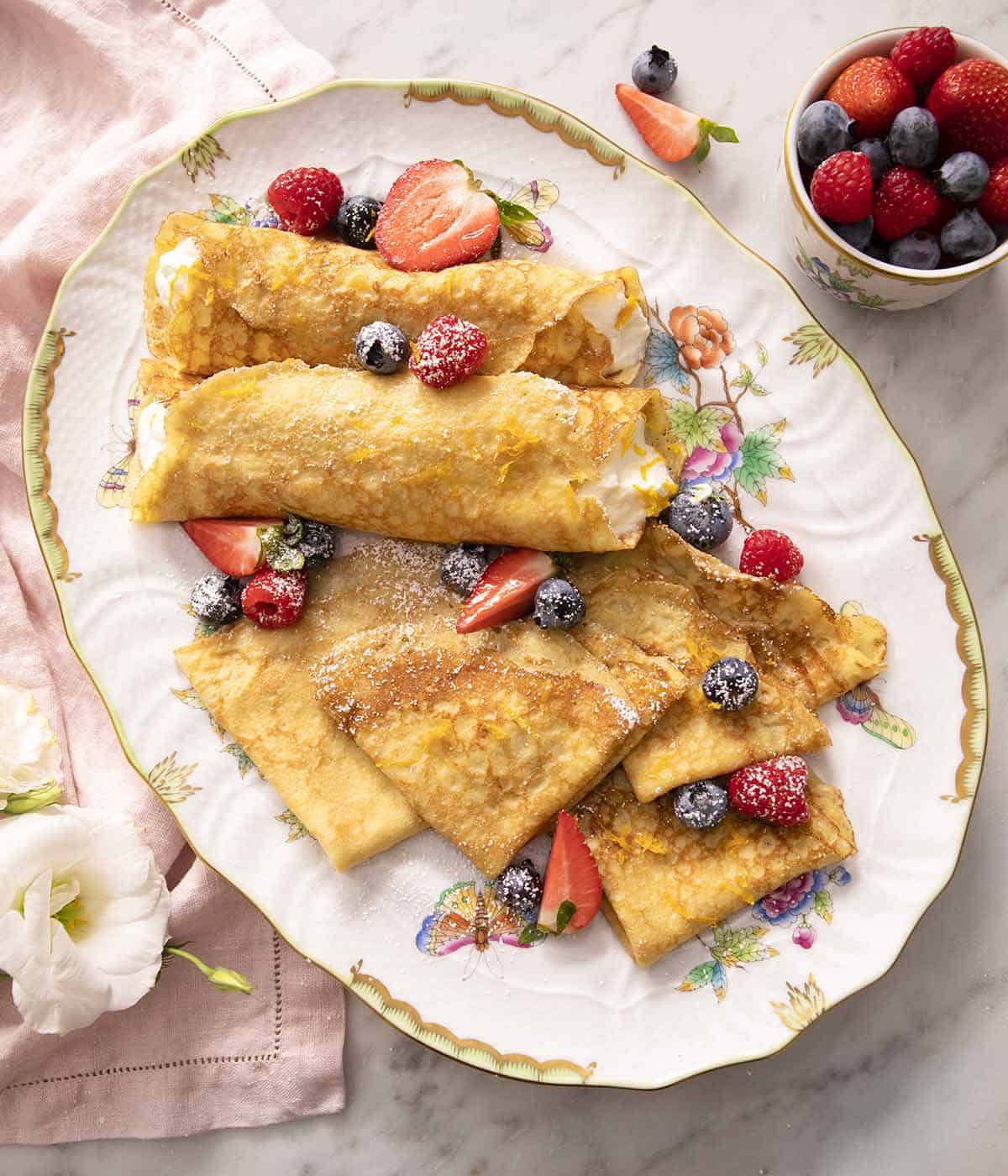 A large platter with crepes and berries on a marble surface.