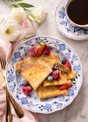 Folded crepes with berries and powdered sugar on a blue and white plate.