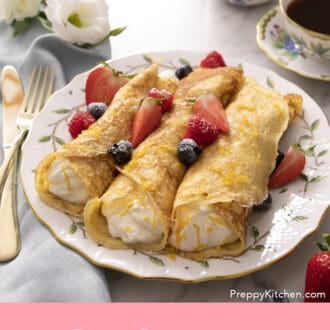 Pinterest graphic of rolled crepes with whipped cream inside on a plate with berries.