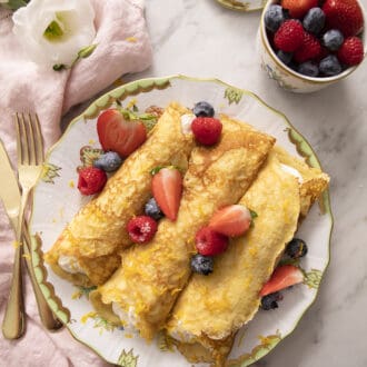 Pinterest graphic of rolled crepes on a plate with berries.