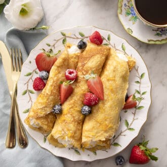 Pinterest graphic of rolled crepes on a plate with berries.