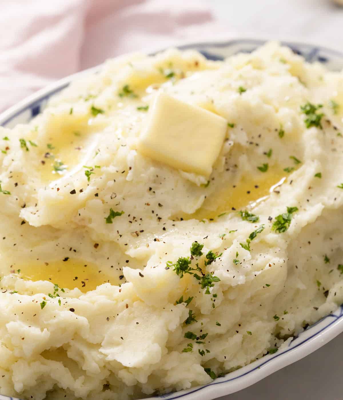 A big serving dish of mashed potatoes with a pat of butter melting on top.