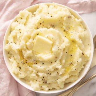 Mashed potatoes with melted butter and cracked pepper in a white bowl.