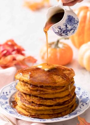 Maple syrup pouring onto a stack of pumpkin pancakes.