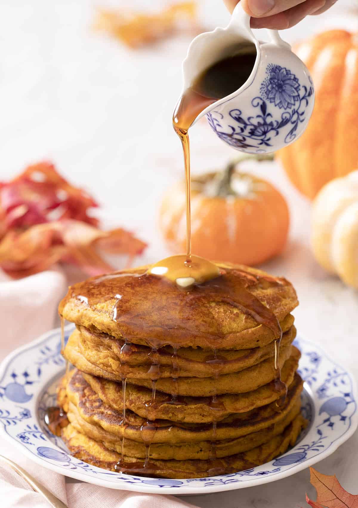 Maple syrup pouring onto a stack of pumpkin pancakes.