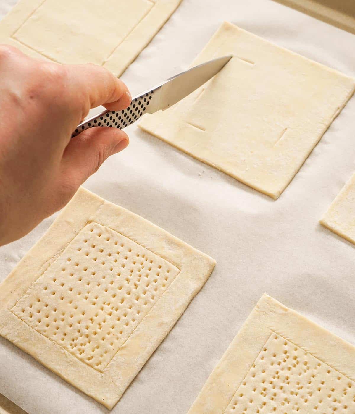 A small knife scoring squares of puff pastry.