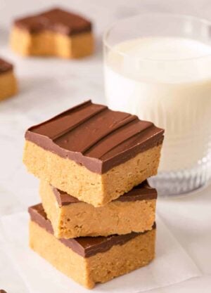 A stack of peanut butter bars on a marble surface alongside a glass of milk.