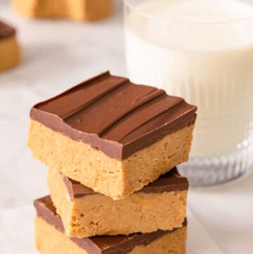 A stack of peanut butter bars on a marble surface alongside a glass of milk.