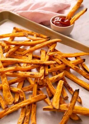 A pile of sweet potato fries on a golden baking sheet.