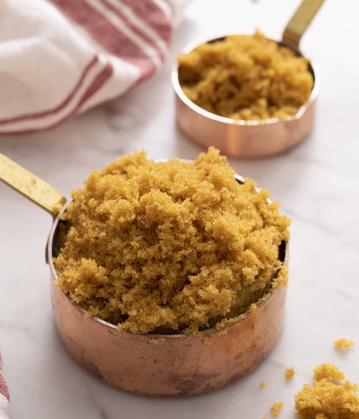 Two copper measuring cups filled with brown sugar.