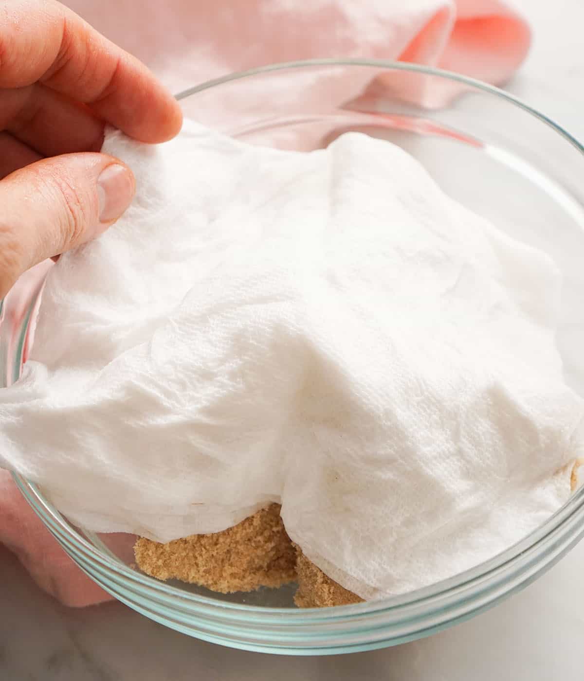 A damp paper towel on a bowl of hard brown sugar.