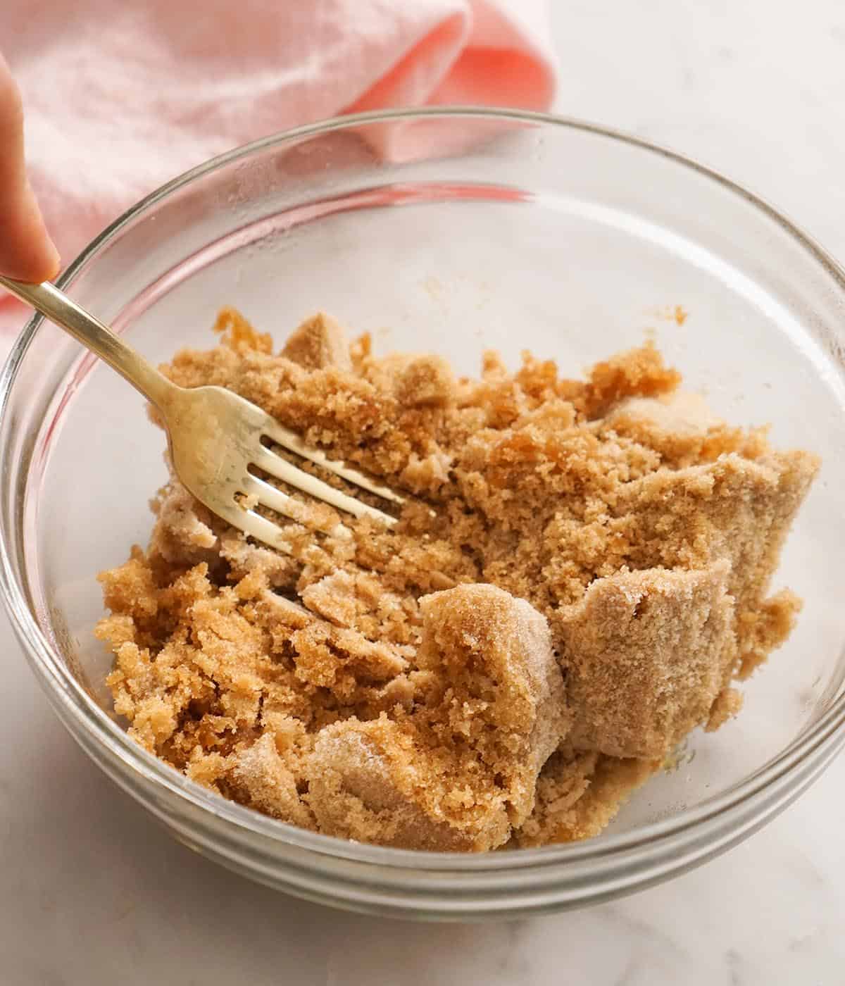 A golden fork breaking up brown sugar after it has been softened.