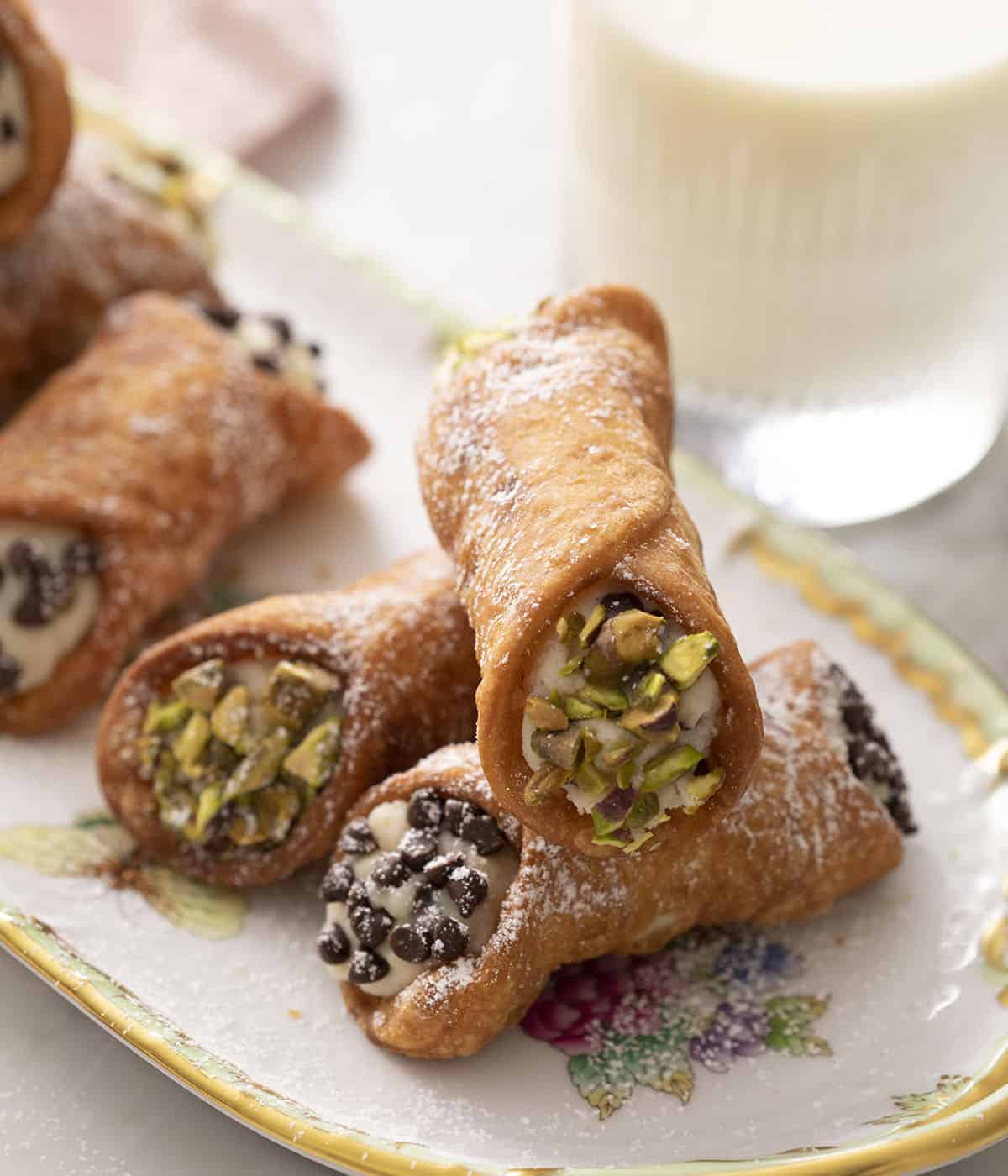 Cannoli with pistachios and chocolate chips next to a glass of milk.