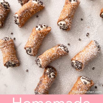 several cannoli sprinkled with powdered sugar spread across white marble counter