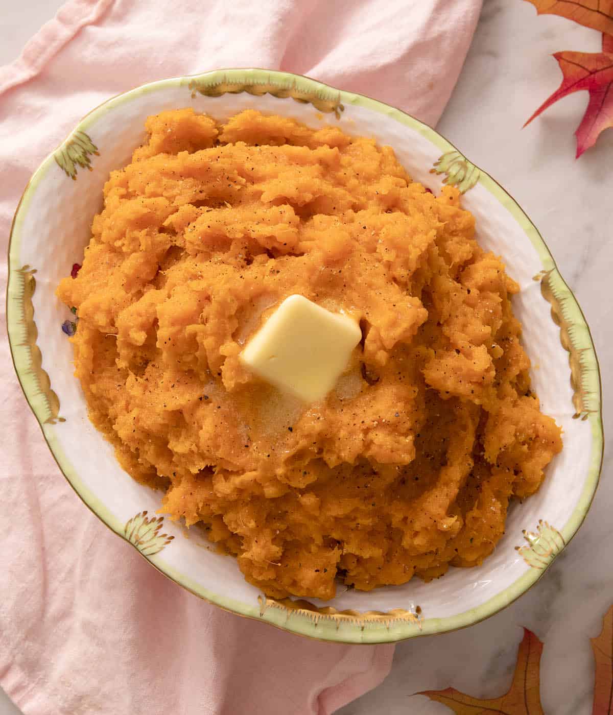 Mashed sweet potatoes in an oval bowl next to a pink linen napkin.