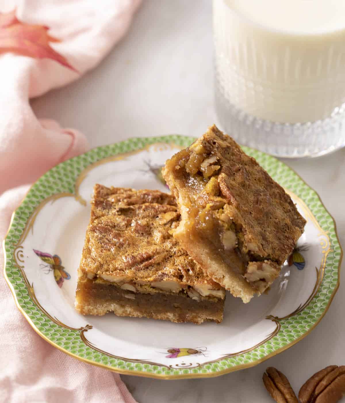 Two pecan pie bars on a plate with a bite taken out of one.