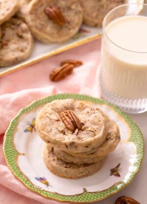 A stack of pecan sandies on a plate next to a glass of milk.