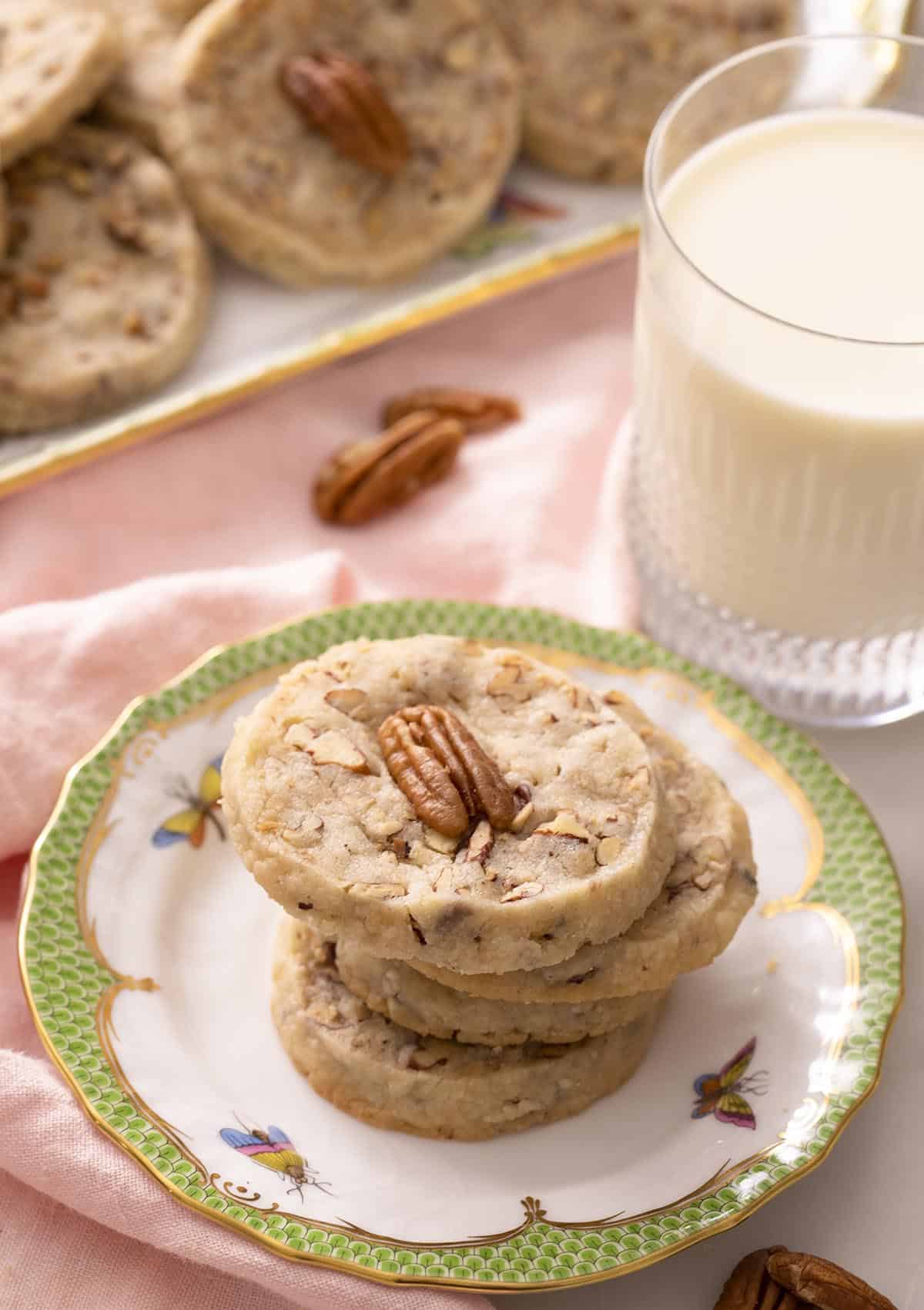 A stack of pecan sandies on a plate next to a glass of milk.