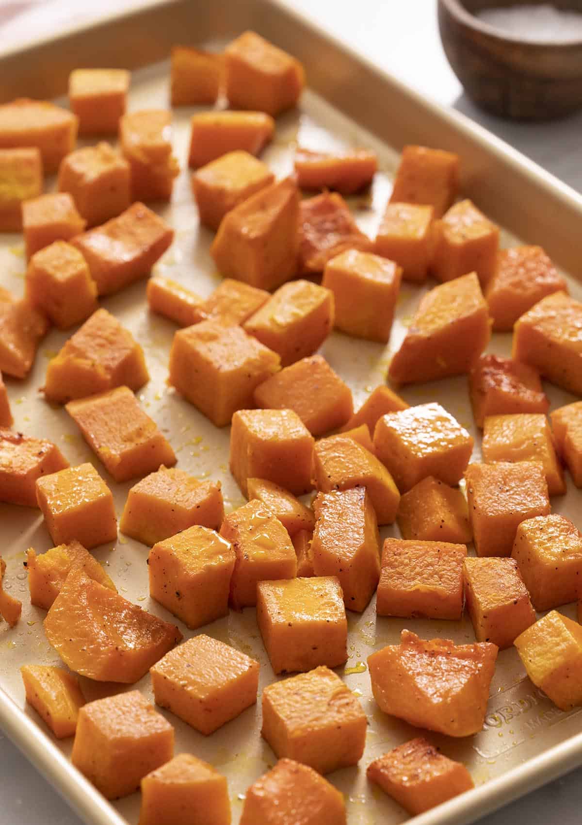Roasted butternut squash pieces on a golden baking sheet.