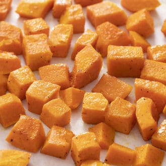 Cubes of roasted butternut squash on a piece of white parchment paper.