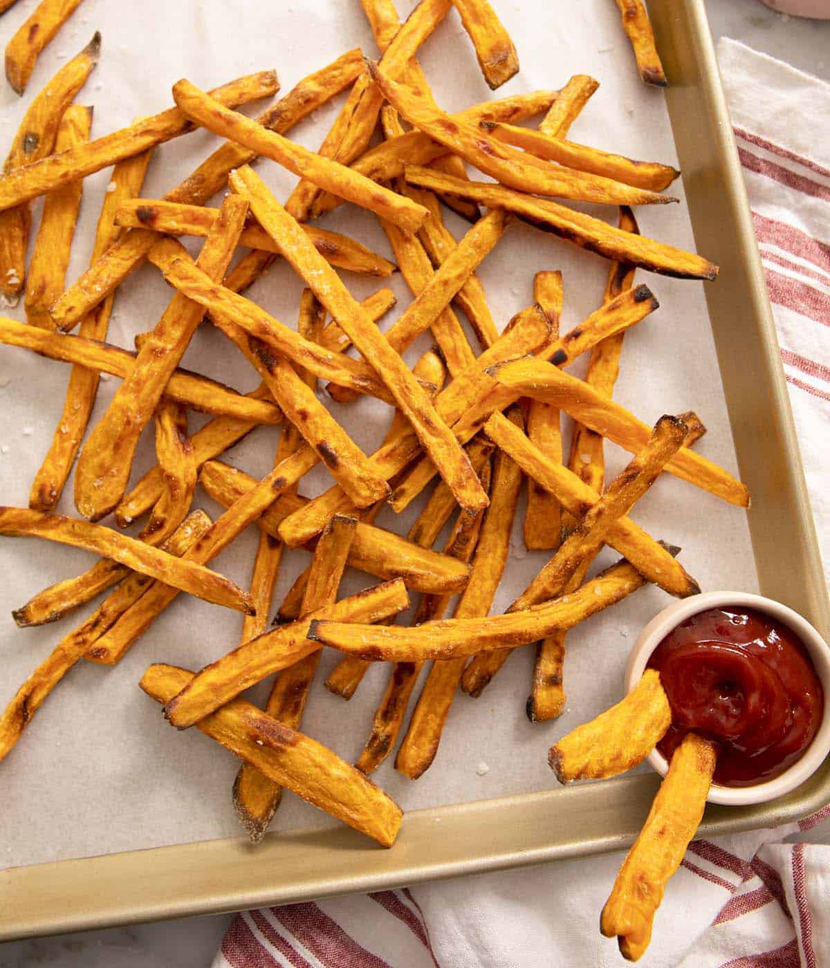 Sweet potato fries on a baking sheet with a small bowl of ketchup.