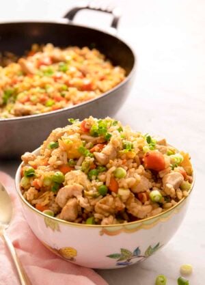 Chicken fried rice in a white bowl with a skillet behind it