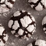 Chocolate crinkle cookies covered in powdered sugar on a grey surface.