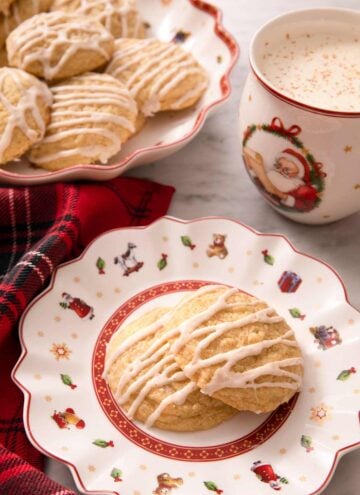 Eggnog cookies on a plate with a mug of hot cocoa behind it