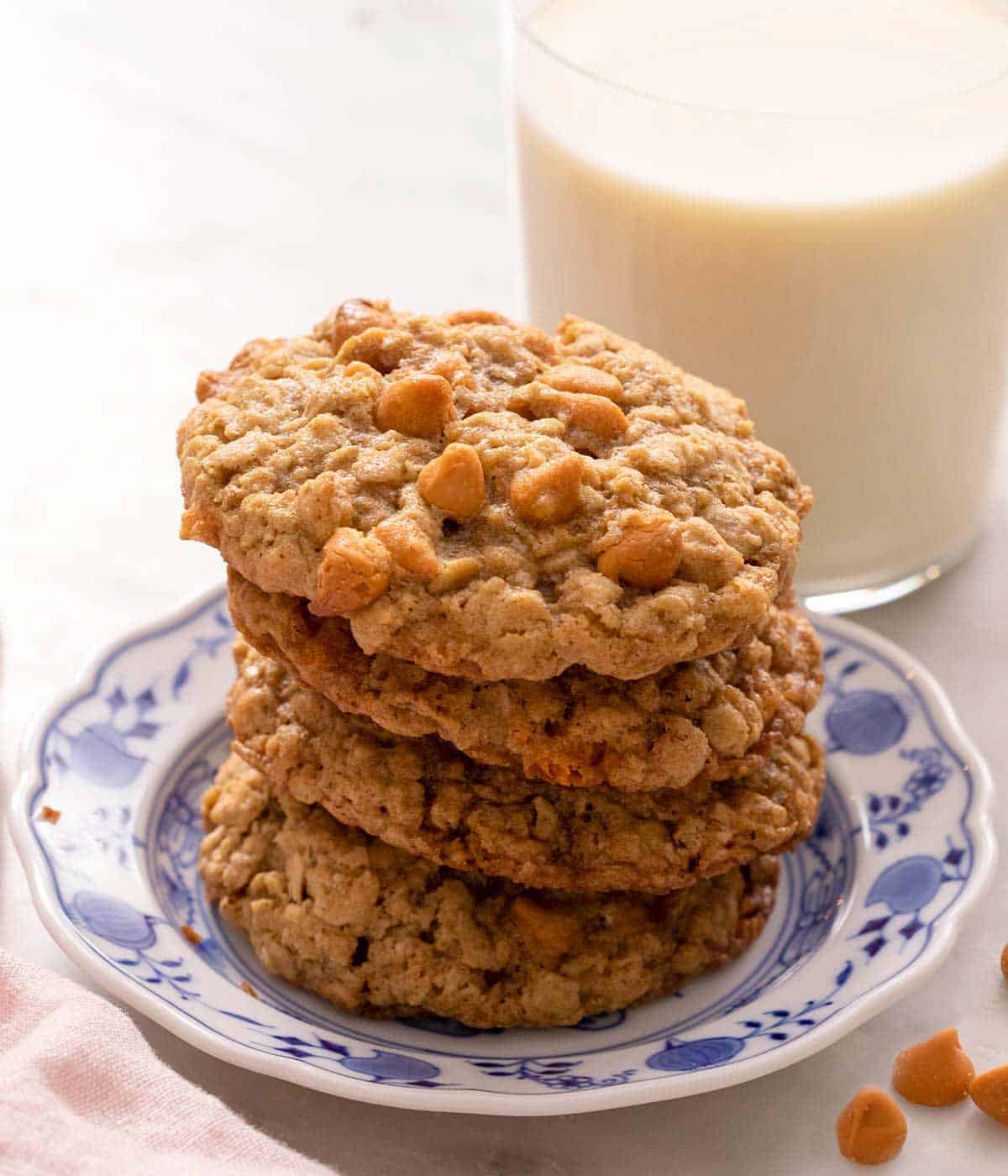 Oatmeal scotchies stacked up on a plate with a glass of milk behind it