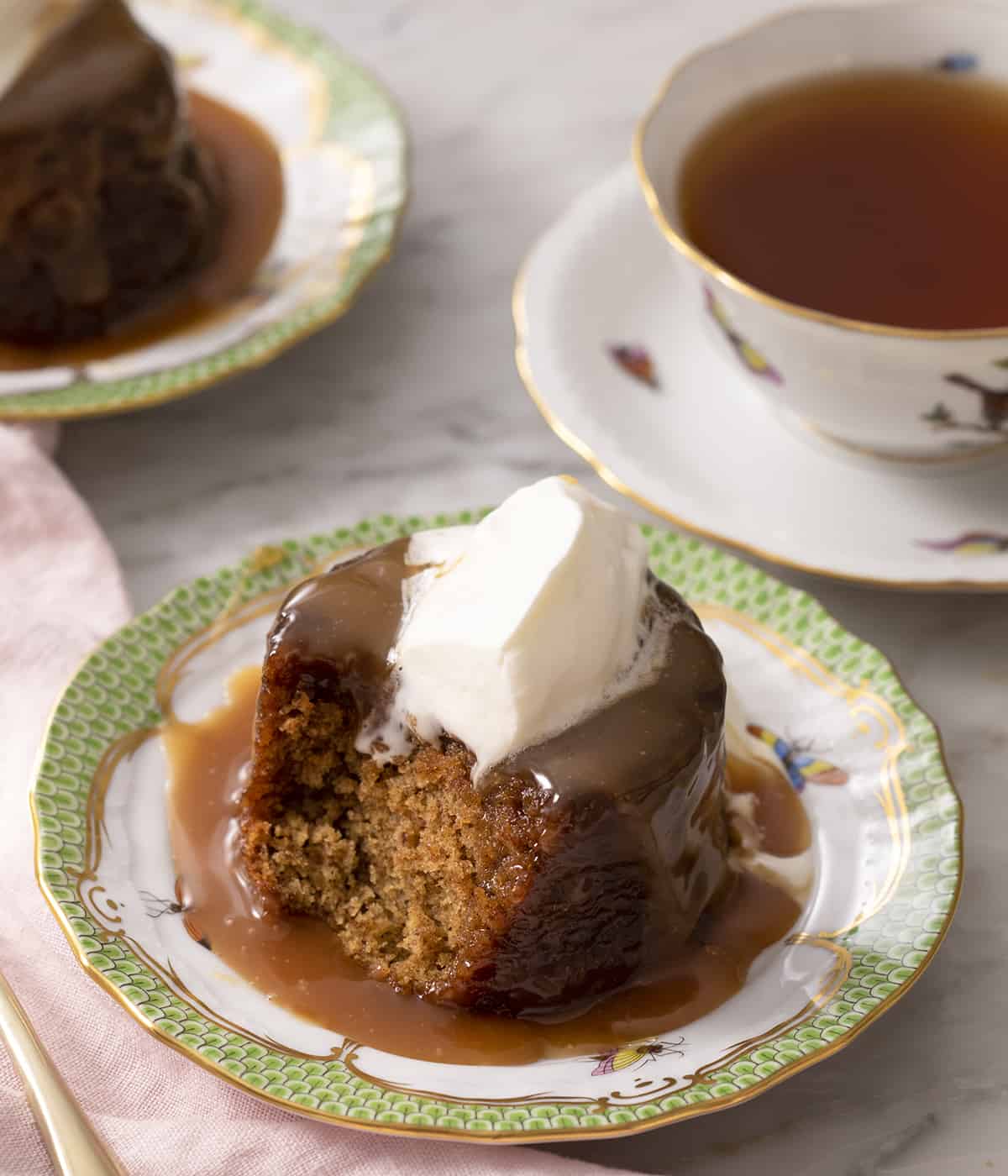 Sticky toffee pudding on a plate topped with cream with a bite out