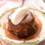 A close up of sticky toffee pudding on a plate topped with whipped cream
