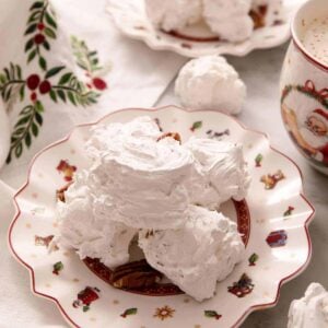 A close up of three pieces of divinity candy on a plate. A mug of hot chocolate and more candy in the background.