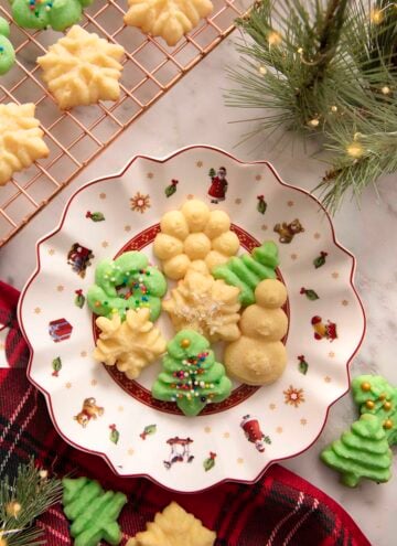 A white and red Christmas plate filled with green and white Christmas cookies.