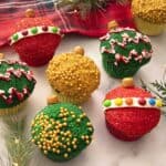 Christmas ornament cupcakes on a marble counter next to some pine sprigs.