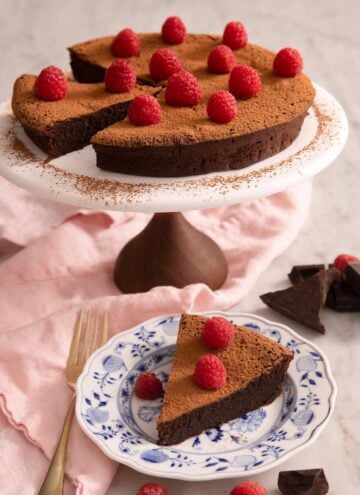 A flourless chocolate cake on a cake stand with a slice on a plate