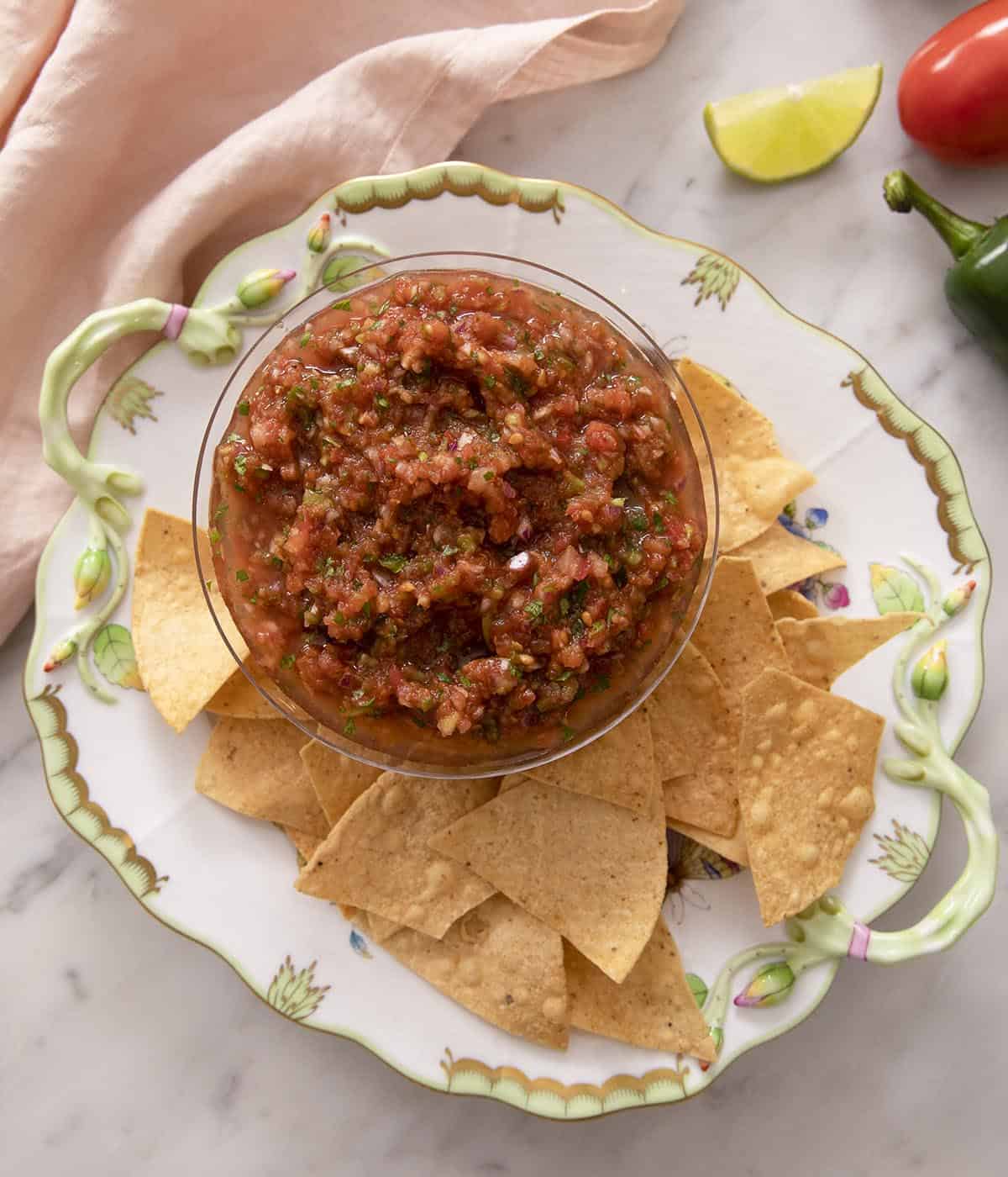 An overhead shot of salsa in a bowl with a bunch of tortilla chips on a plate beside it