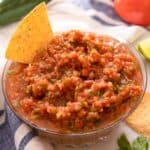 A close up of a bowl of salsa with a chip dunked into it