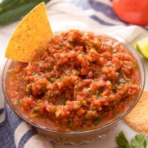 A close up of a bowl of salsa with a chip dunked into it.