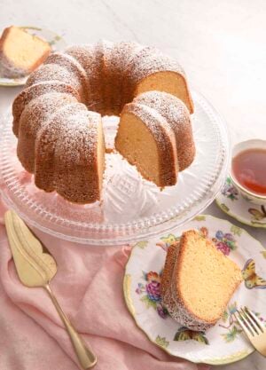 Sour cream pound cake on a cake stand with a slice on a plate.