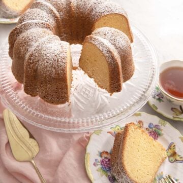 Sour cream pound cake on a cake stand with a slice on a plate.
