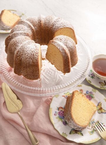 A sour cream pound cake on a cake stand with a slice on a plate