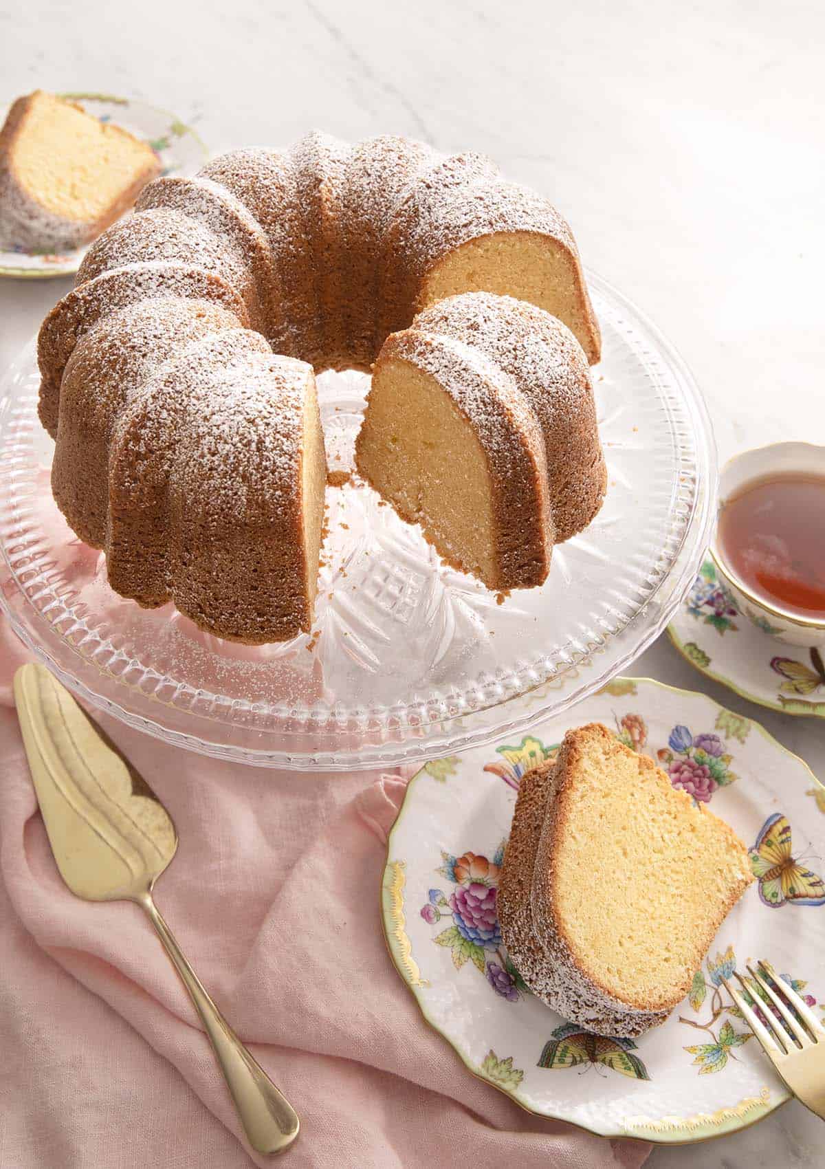 A sour cream pound cake on a cake stand with a slice on a plate