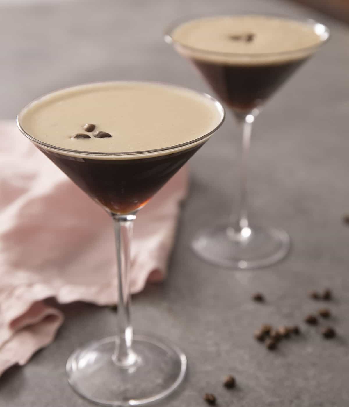 Two espresso martinis in martini glasses topped with coffee beans